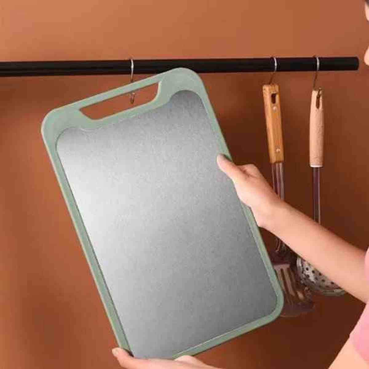 Main tenant une planche à découper grise et verte avec une poignée ergonomique, idéale pour préparer de grands repas
