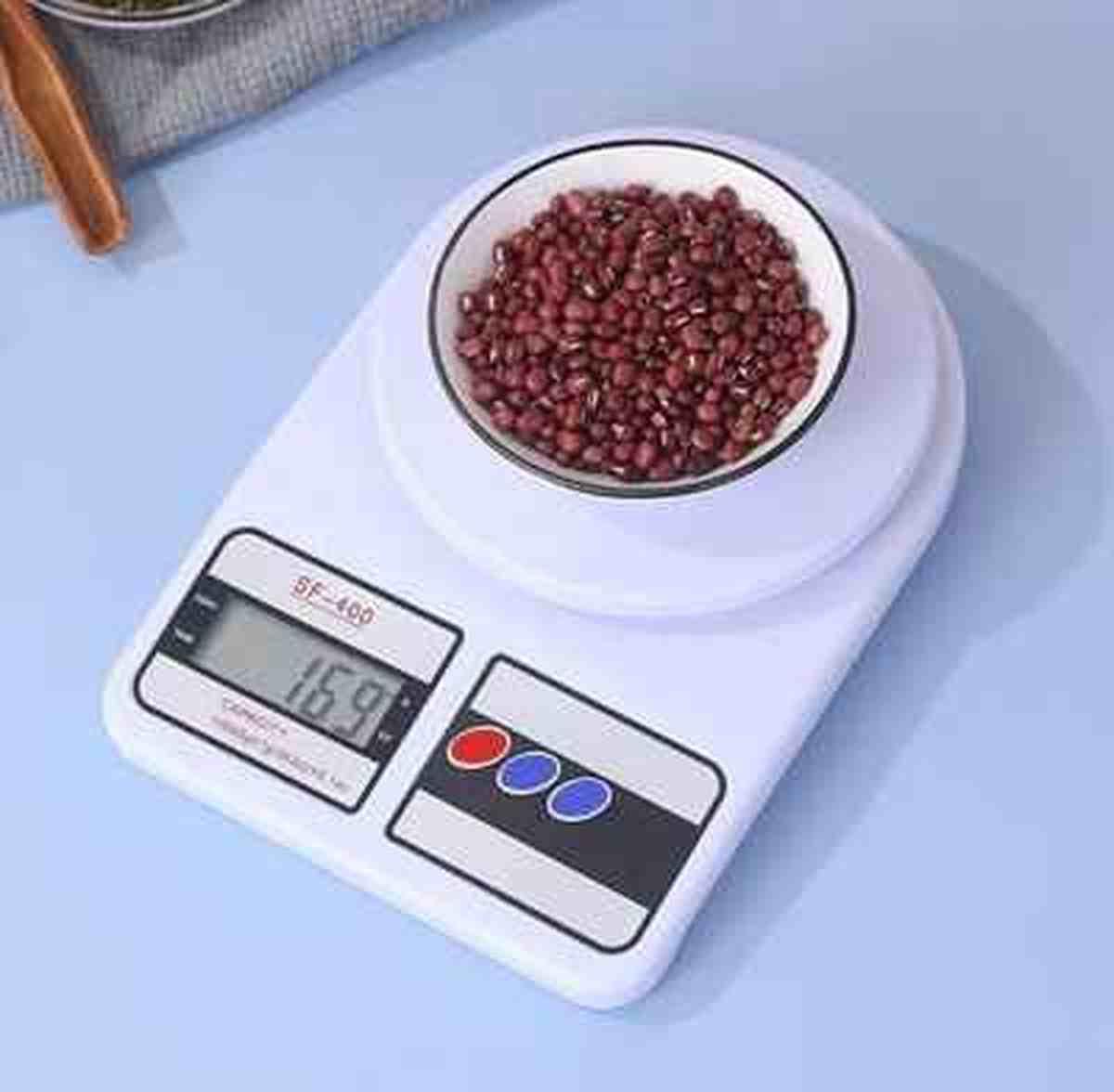 Gros plan d'une balance Precision Pro affichant 169g pour un bol de haricots rouges sur un fond bleu clair esthétique.