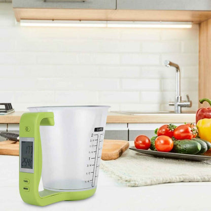 Balance de cuisine verte avec tasse mesureuse posée sur un plan de travail en bois dans une cuisine lumineuse avec des légumes frais en arrière-plan.