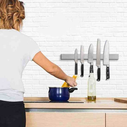 Personne cuisinant à côté d'une barre aimantée en acier inox fixée sur un mur de briques, avec plusieurs couteaux de cuisine à portée de main.