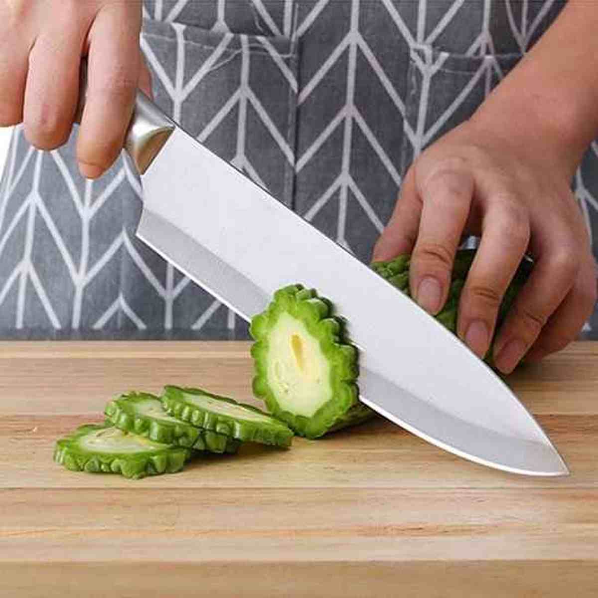 Utilisation d'un couteau de chef japonais en acier inoxydable pour trancher finement un légume vert sur une planche en bois.