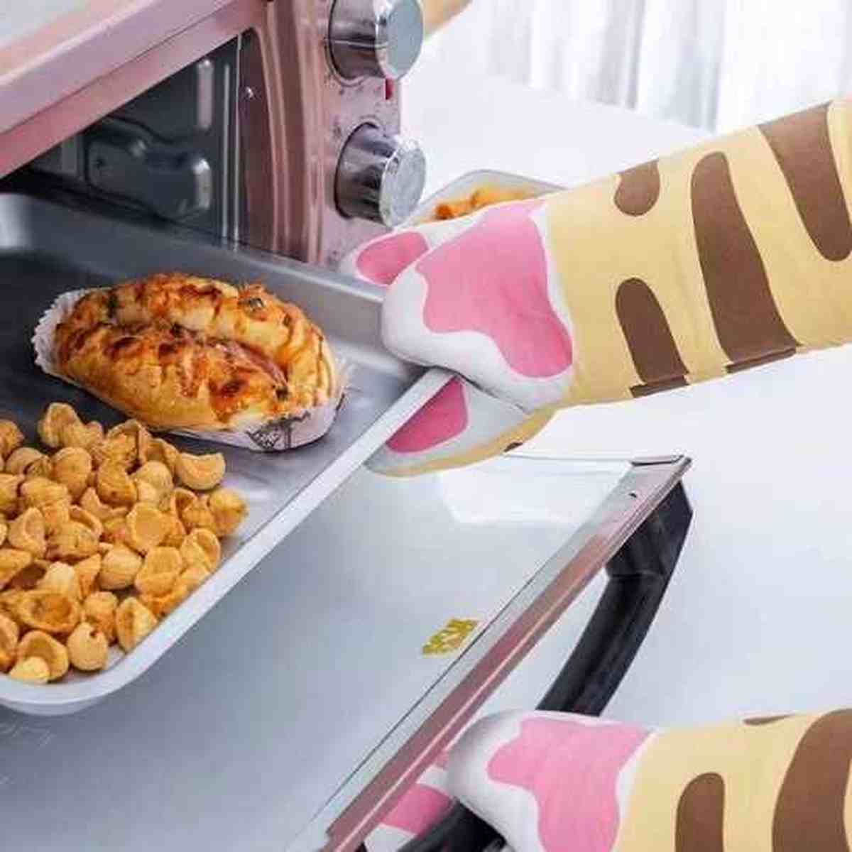 Gants de cuisine beiges à motifs de pattes roses utilisés pour retirer une plaque de cuisson du four, offrant une protection thermique optimale.