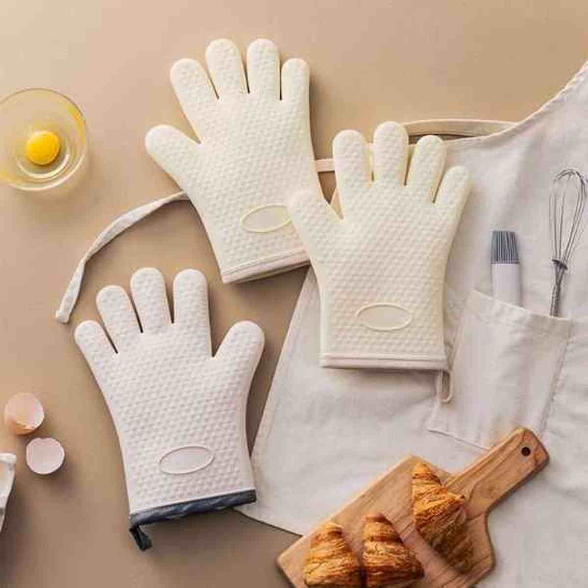 Gants de cuisine ThermoProtect en silicone beige posés sur un plan de travail avec des croissants frais, illustrant la protection thermique pour la cuisson au four.