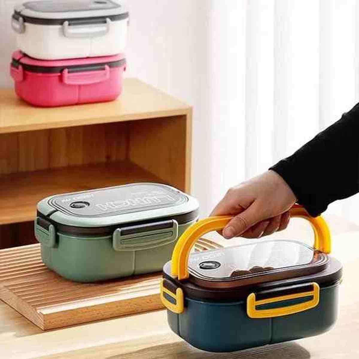 Main tenant une lunch box éco-étanche par sa poignée intégrée, avec plusieurs modèles de différentes couleurs en arrière-plan