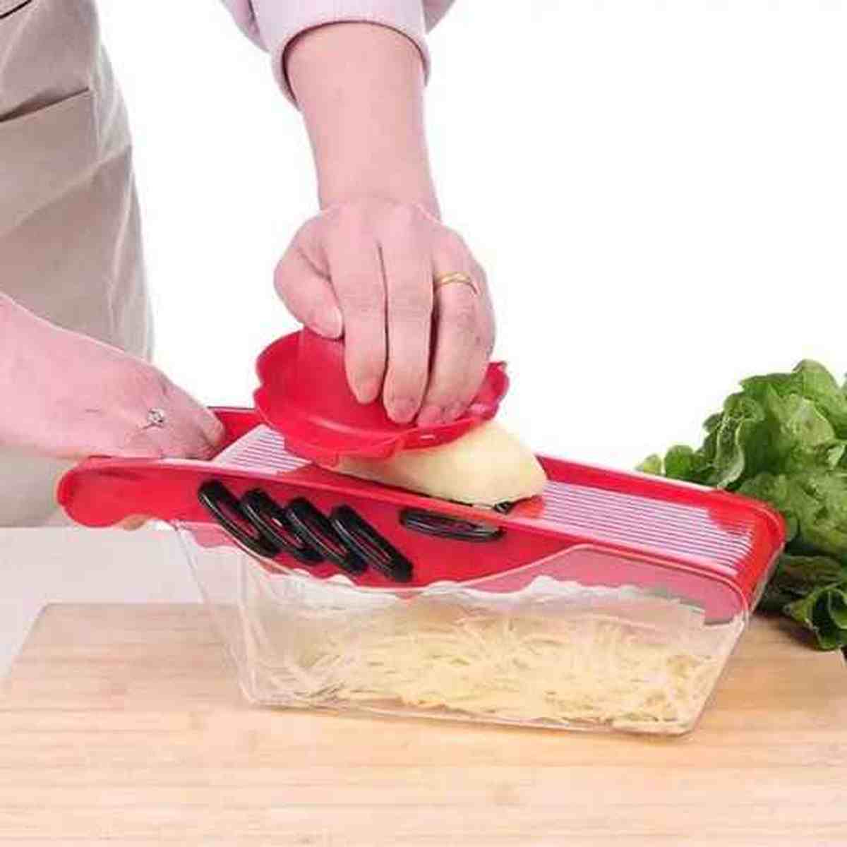 Utilisation du poussoir de sécurité de la mandoline de cuisine rouge pour râper des aliments sans risque pour les mains.