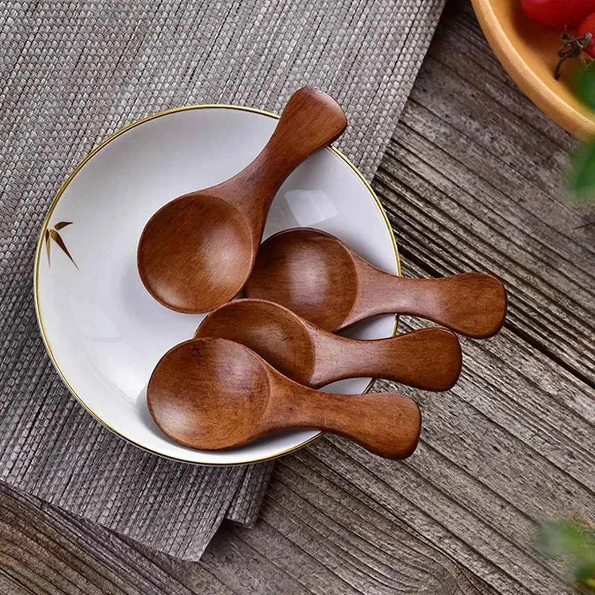 Quatre mini cuillères de dosage en bois sombre présentées élégamment sur une petite assiette en céramique blanche, style cuisine naturelle