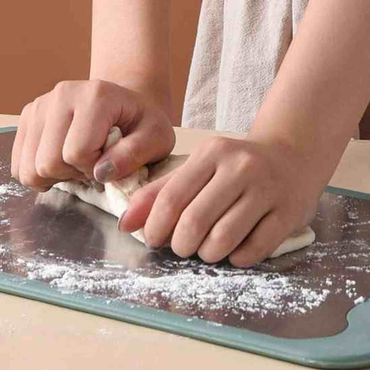 Personne pétrissant de la pâte à pain sur la planche à découper robuste, illustrant sa stabilité et sa grande surface de travail
