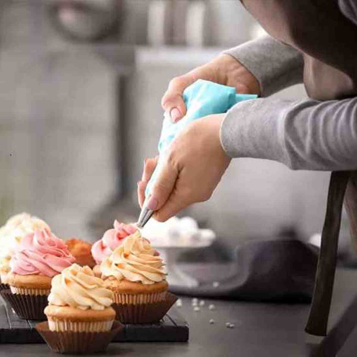 Poche à douille en silicone bleu PâtissiPro utilisée pour glacer des cupcakes avec une crème onctueuse, mettant en avant la précision du kit professionnel.