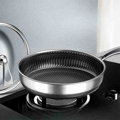 Poêle en acier inoxydable sur une plaque de cuisson à gaz, montrant la structure alvéolée et le couvercle en verre transparent.