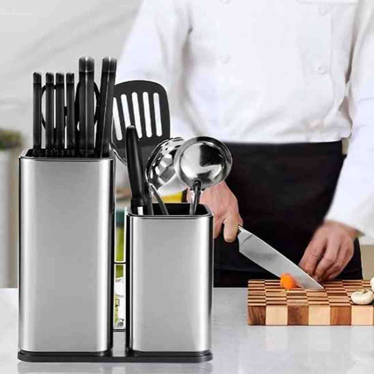 Chef cuisinier utilisant un couteau à côté de l'organisateur en acier inoxydable contenant couteaux et ustensiles de cuisine.