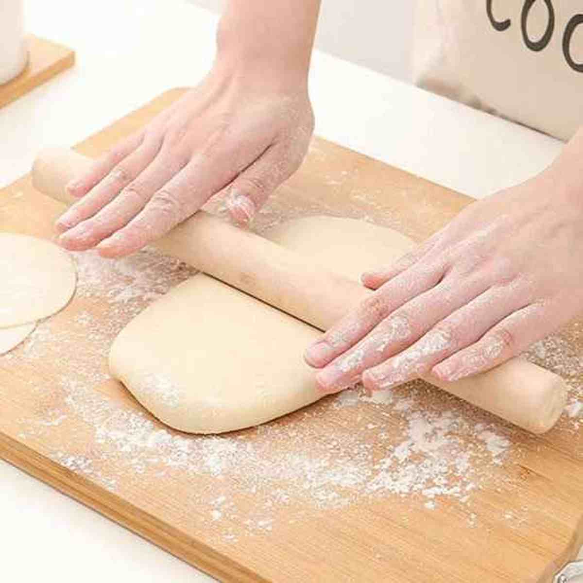 Rouleau à pâtisserie Artisan Pro en bois massif étalant une pâte épaisse sur une planche en bois farinée