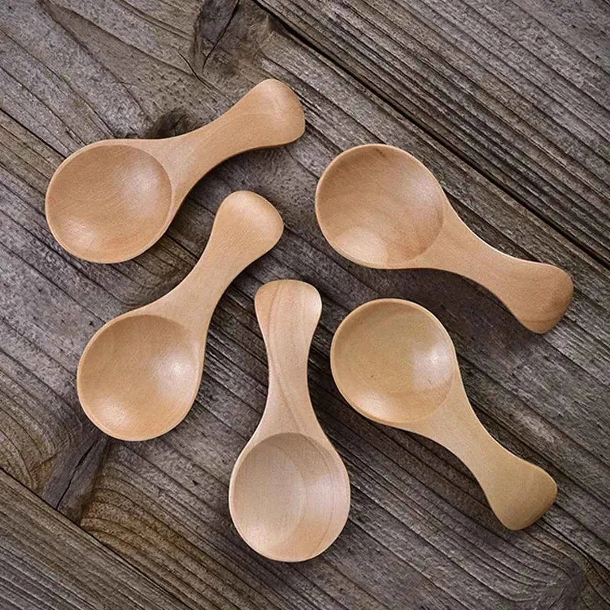 Alignement de cinq mini cuillères de dosage en bois naturel posées sur une surface en bois brut, montrant la finition lisse et artisanale