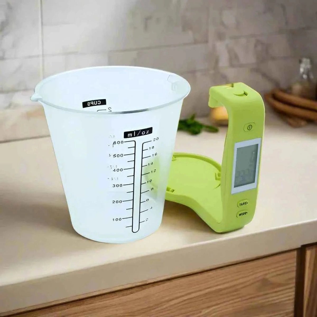 Gros plan sur la tasse mesureuse transparente graduée en ml et oz, fixée sur le socle de la balance de cuisine électronique verte.